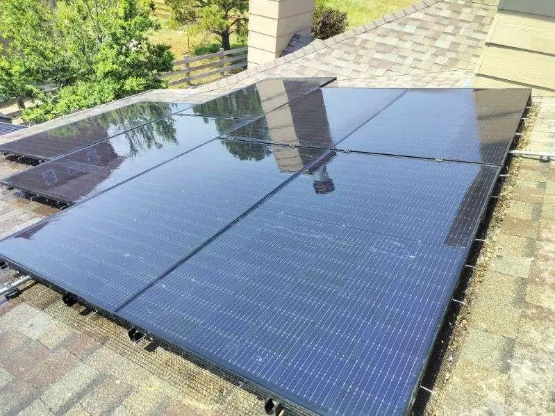 Solar panels installed on a shingled rooftop under clear blue sky with an orange bucket and tools nearby.