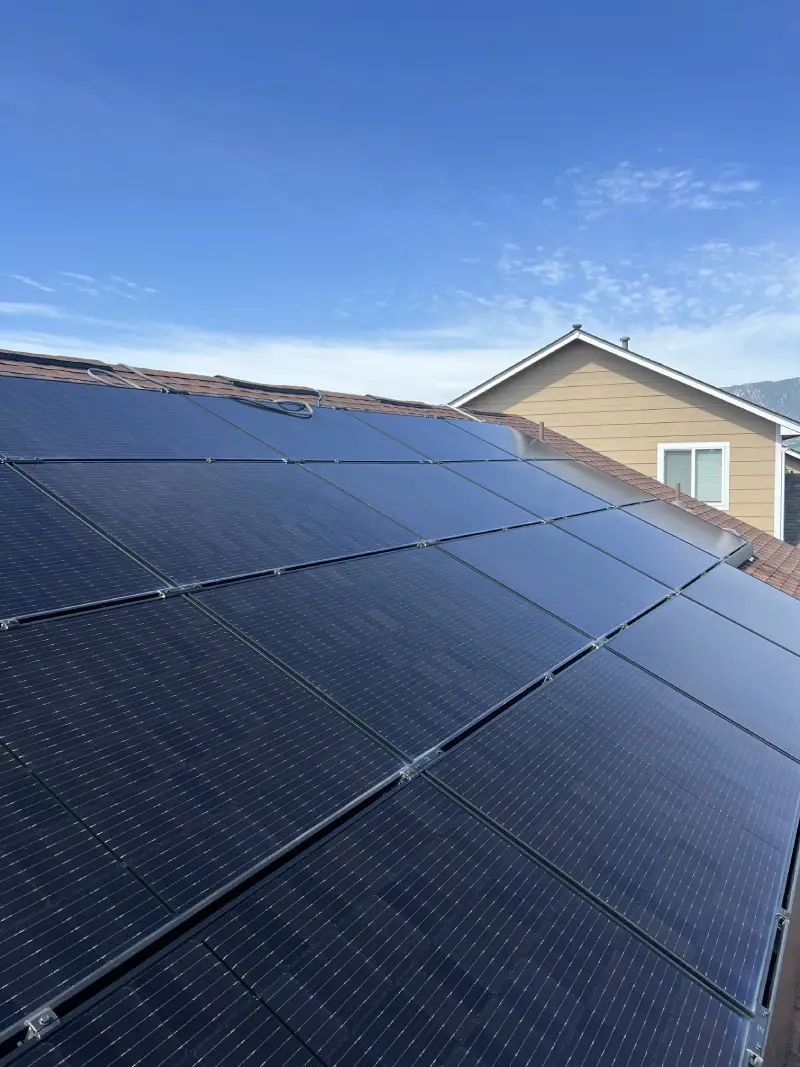 Black solar panels installed on a sloped residential roof under a clear blue sky.