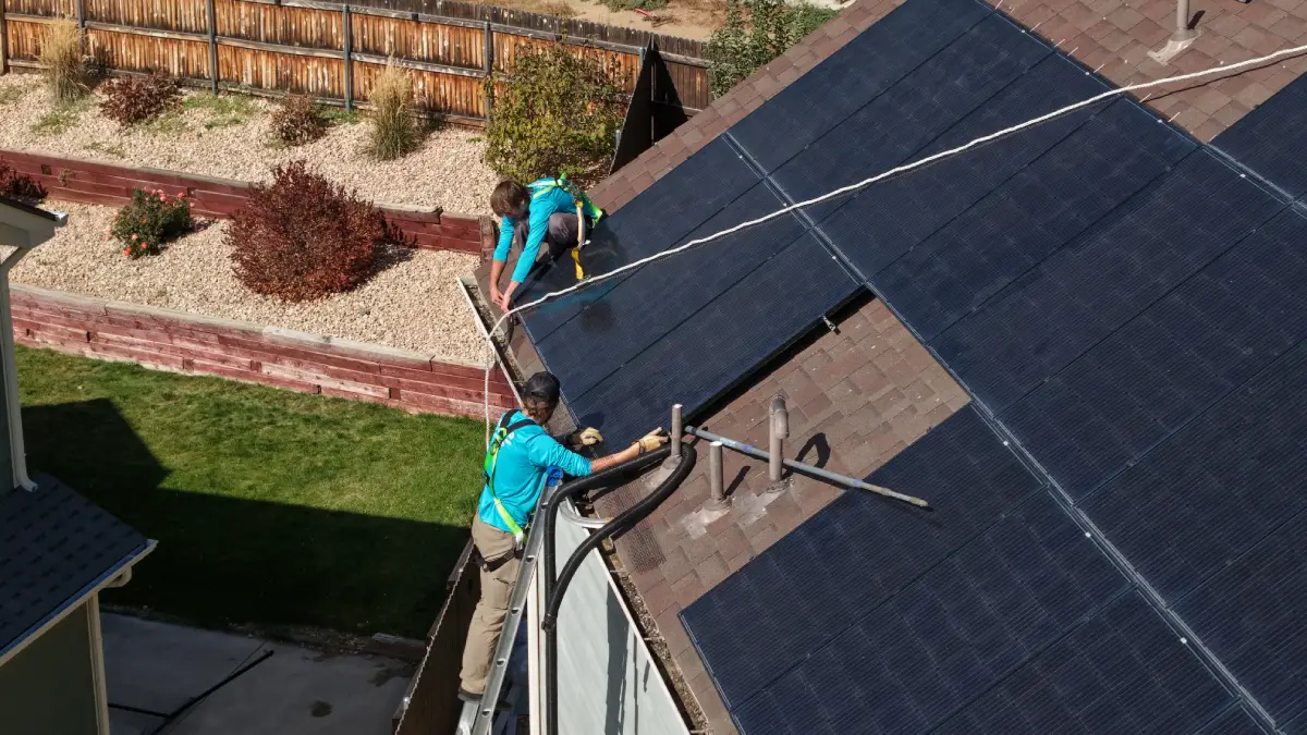 Array of solar panels installed on a rooftop under a clear blue sky with a neighboring house in the background.